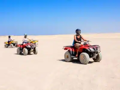 Sunset Quad Safari Trip Marsa Alam with riders crossing golden dunes against a glowing orange sunset sky