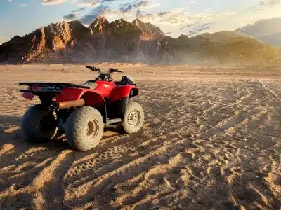 Sunset Quad Safari Trip Marsa Alam with riders crossing golden dunes against a glowing orange sunset sky